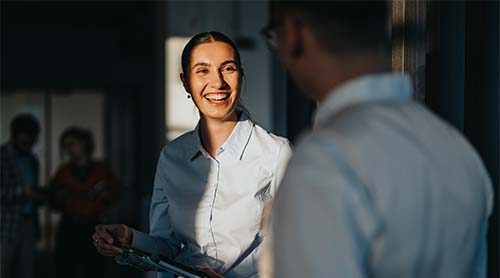 A diverse group of business people engaging in a friendly conversation in an office hallway. The image captures a positive and collaborative work environment with multicultural colleagues.